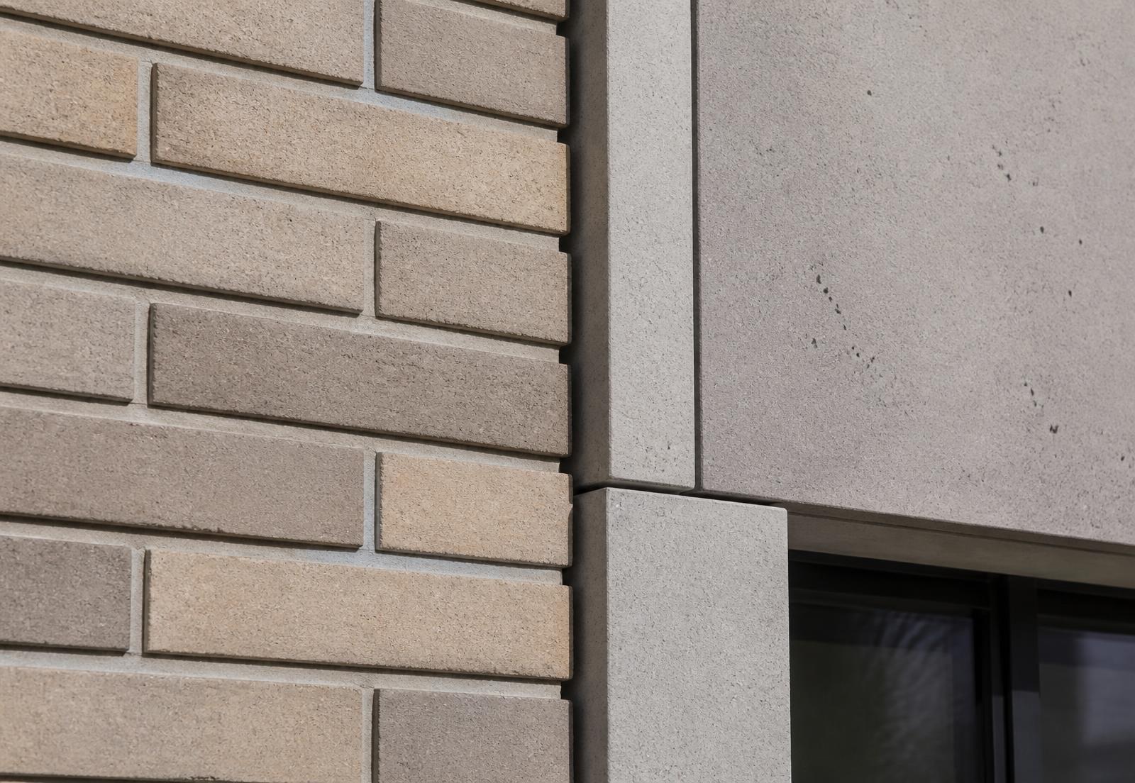 Detail of a completed facade showing brick slip cladding meeting a cast stone reveal and a window head