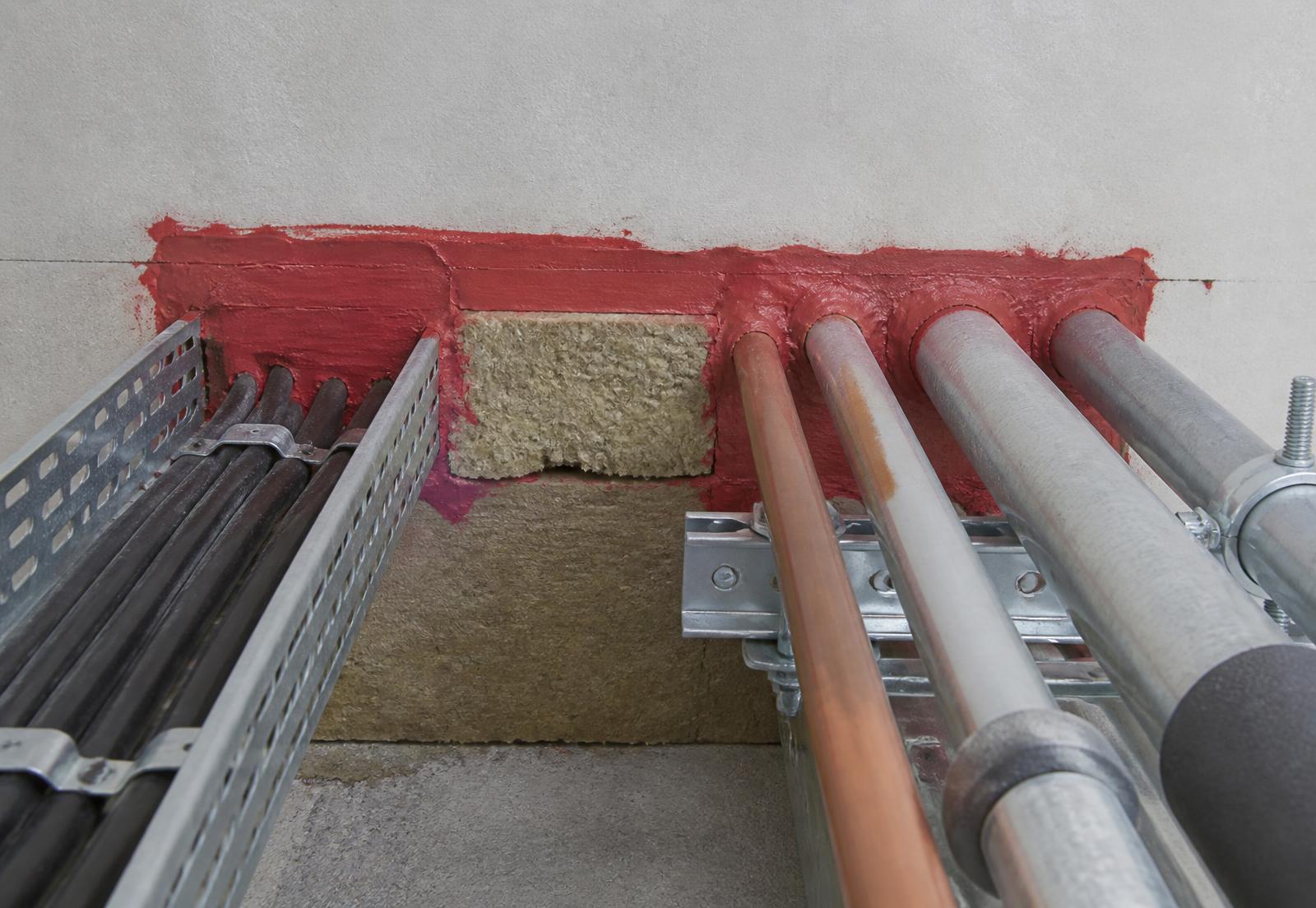 Fire stopping installation detail showing intumescent sealant and mineral wool around service penetrations through a compartment wall