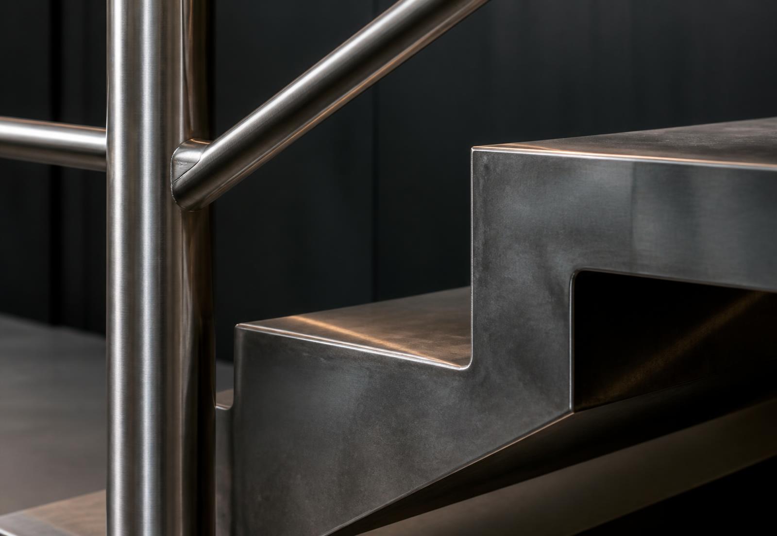 Detail of architectural metalwork showing a brushed stainless steel handrail junction and a folded steel stair edge